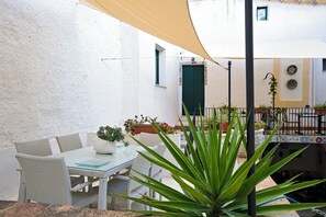 Pátio externo com móveis de vime, mesa e vasos de plantas.