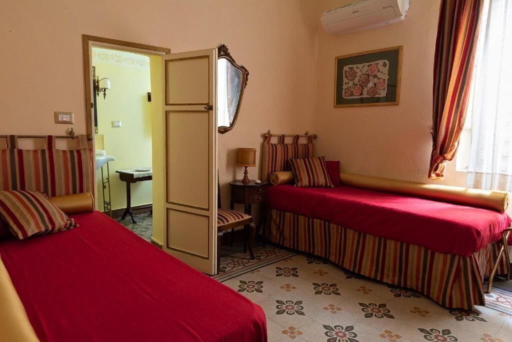 A hotel room with two beds, a bathroom, a mirror, a picture on the wall, and a window with curtains.