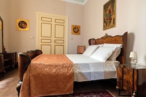 Een slaapkamer met een bed, een houten nachtkastje, een stoel, een deur en twee ingekaderde foto's aan de muur.
