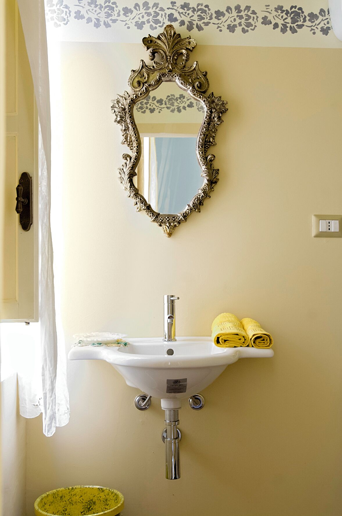 Een badkamer met een witte wastafel, een decoratieve spiegel en gele handdoeken.