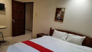 A hotel room with a bed, a nightstand, a small table, and a door leading to another room. - GW Furama Apartment (Kuching)