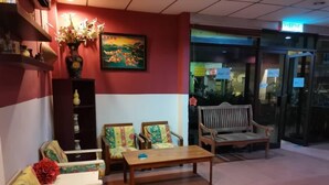 A lobby with a reception desk, two sofas, a bench, and a vase of flowers. - GW Furama Apartment (Kuching)