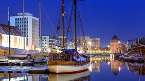A harbor at dusk with a sailing ship docked, buildings in the background, and calm water reflecting the scene. - Marina Club Hotel (Gdansk)
