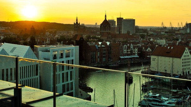 A cityscape at sunset with a river, boats, and buildings. - Marina Club Hotel (Gdansk)