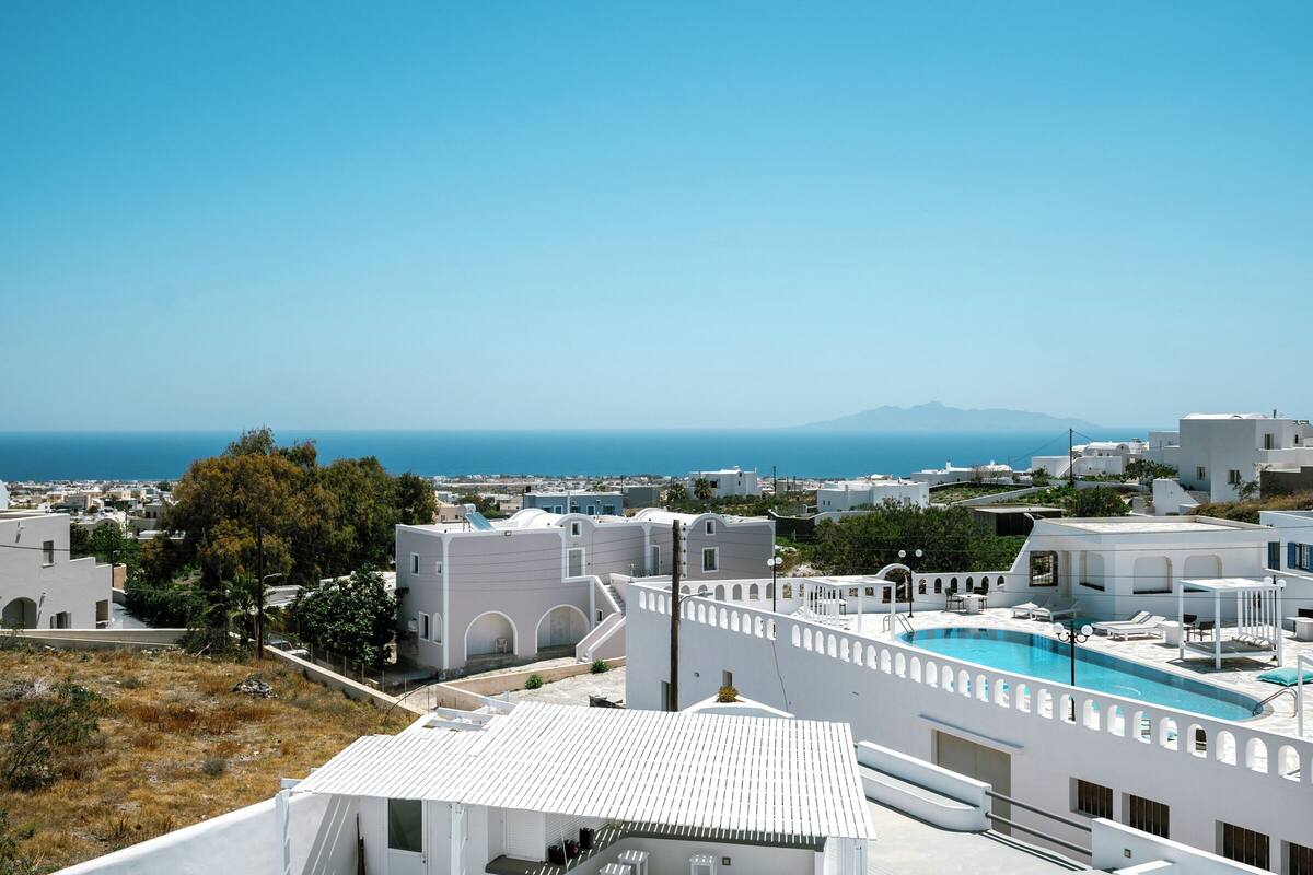 Un bâtiment blanc doté d’une piscine sur le toit, entouré d’autres bâtiments blancs et offrant une vue dégagée sur la mer.