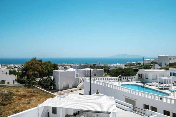 A white building with a rooftop pool, surrounded by other white buildings and a clear view of the sea.