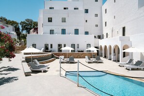 A pool area with lounge chairs and umbrellas, surrounded by white buildings with multiple windows.