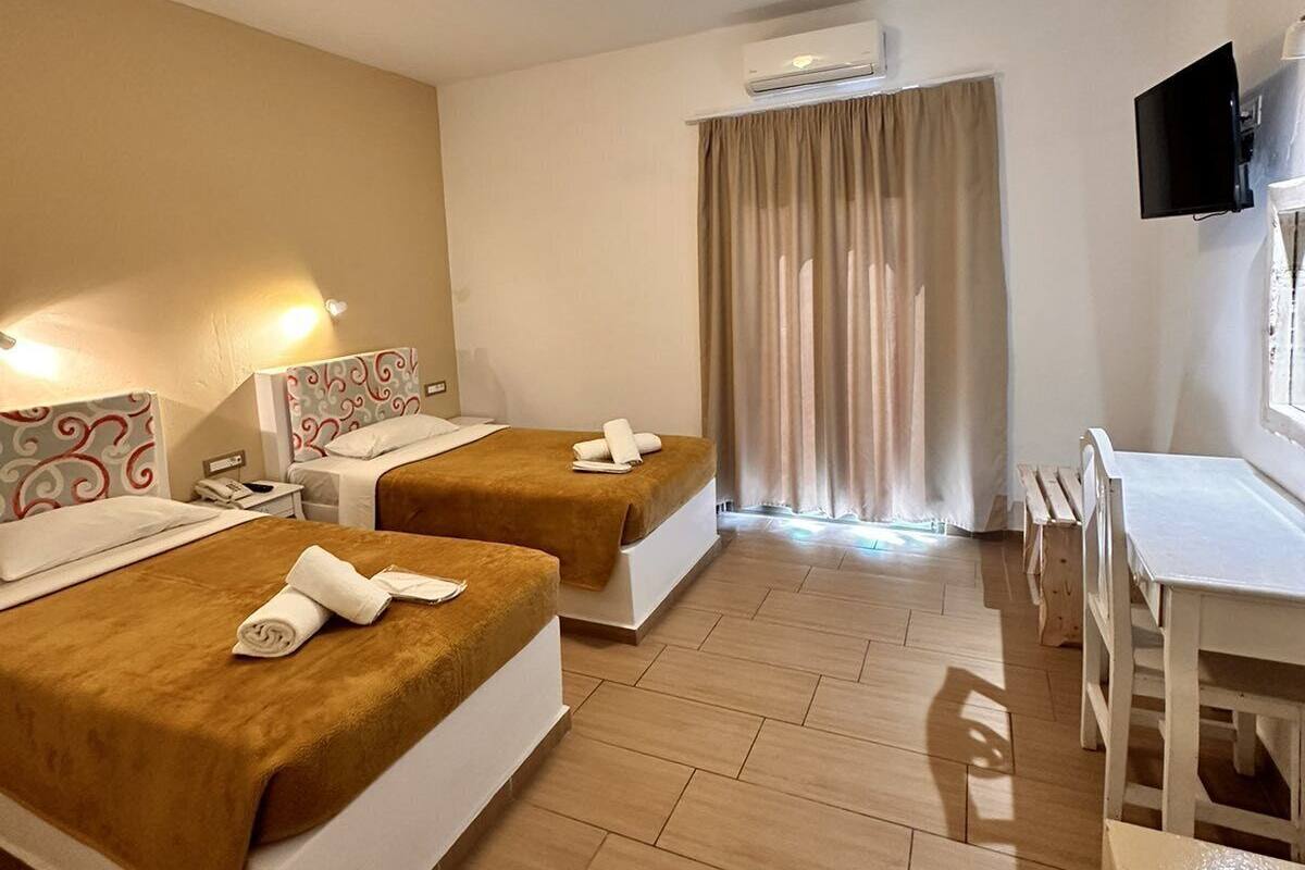 Une chambre d’hôtel avec deux lits, un bureau, une chaise, une télévision et un appareil de climatisation.