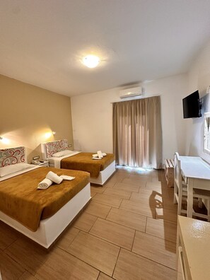 A hotel room with two beds, a desk, a chair, a TV, and an air conditioning unit.