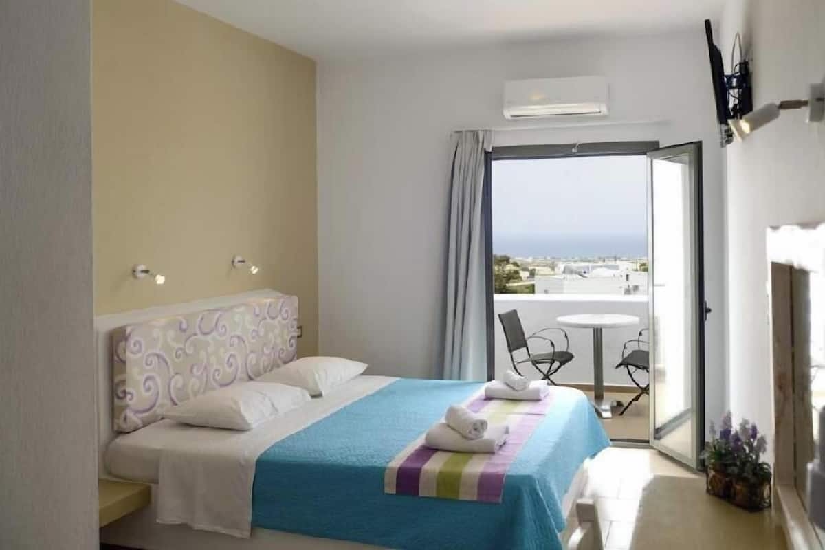 Une chambre d’hôtel comprenant un lit, une petite table avec des chaises, un balcon avec vue et un appareil de climatisation.