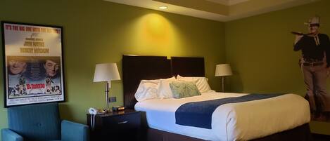 A hotel room with a large bed, two bedside lamps, a nightstand with a phone, a poster on the wall, and a chair.