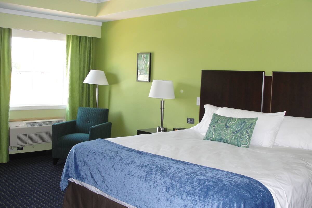 Ein Hotelzimmer mit einem Bett, zwei Stühlen, einem Schreibtisch, einer Lampe und einem Fenster mit Vorhängen.