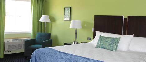 A hotel room with a bed, two chairs, a desk, a lamp, and a window with curtains.