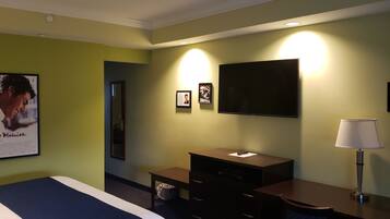 Habitación de hotel con cama, escritorio, silla, televisor, lámpara y un cartel en la pared.