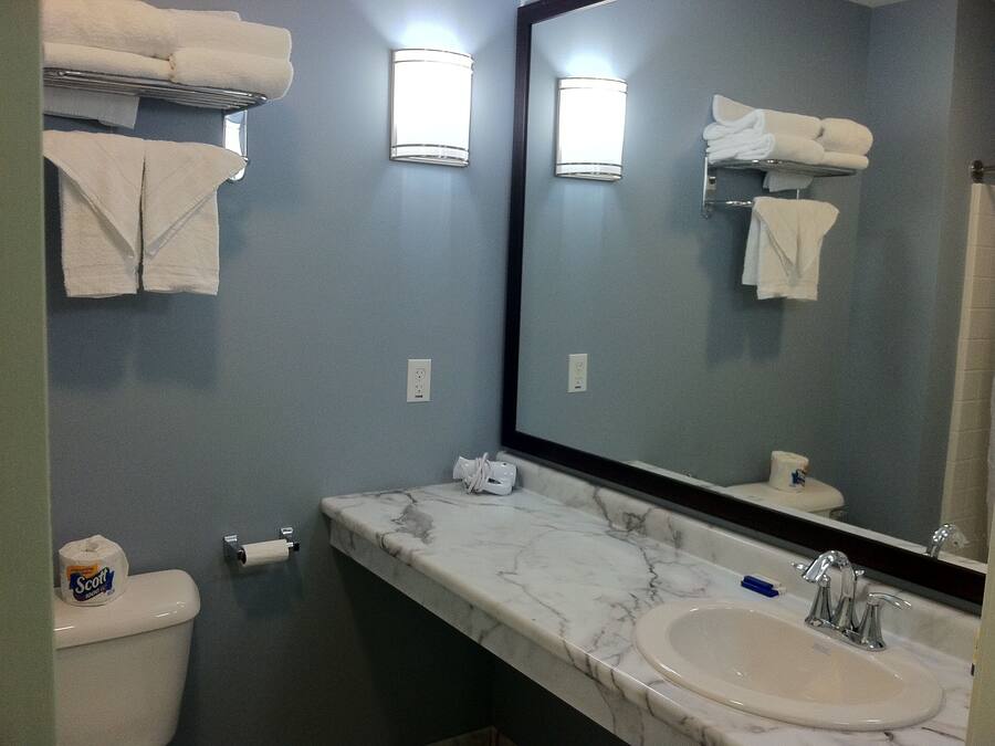 A bathroom with a toilet, sink, and large mirror. There are towels on a rack and a roll of toilet paper on the wall.