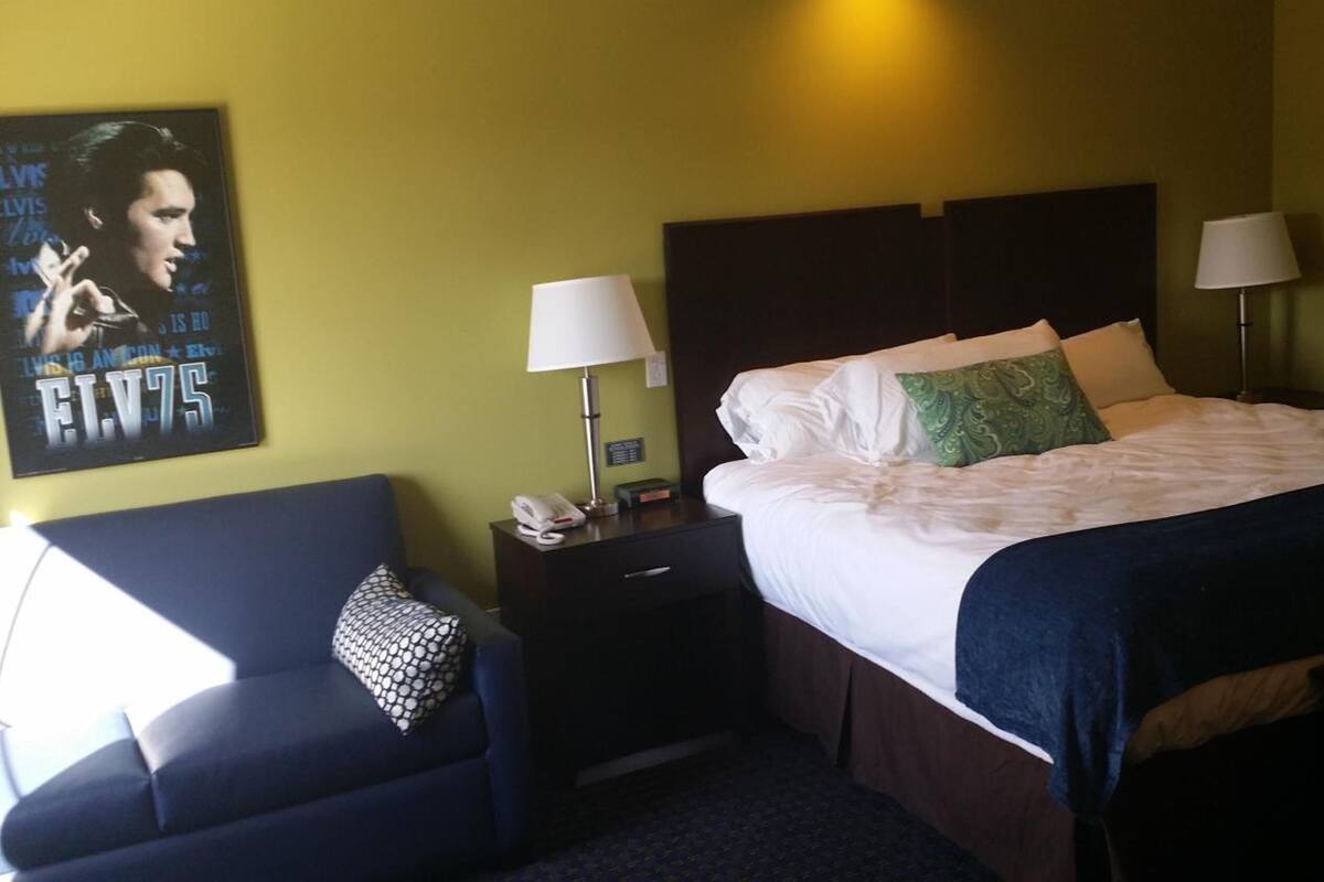 Ein Hotelzimmer mit Bett, Nachttisch, Lampe, Telefon, einem Poster an der Wand und einem Sofa.