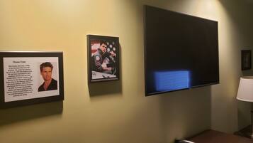A framed biography of actor Thomas Cruise on a wall, a television mounted above it, and a lamp on a table beside the TV.