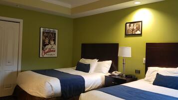 Una camera d'albergo con due letti, un comodino con una lampada, un poster appeso al muro e un quadro incorniciato.