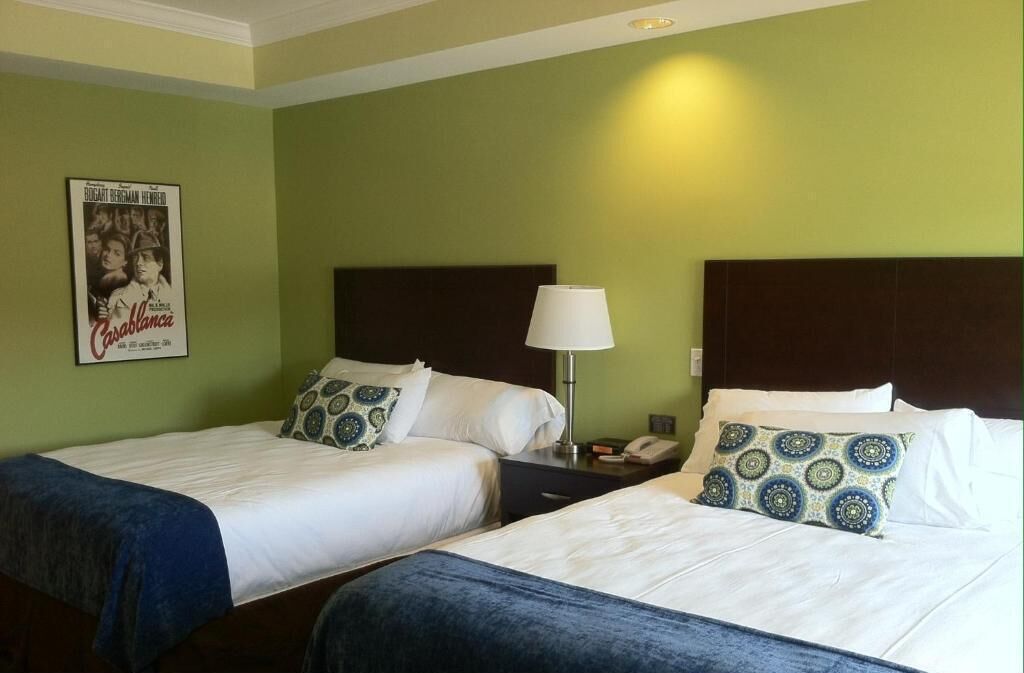 Habitación de hotel con dos camas, una mesita de noche con lámpara y un cartel en la pared.