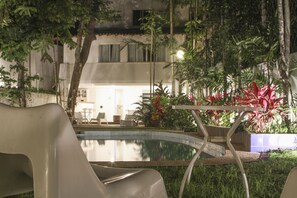 A poolside area with a modern chair, a small table, and lush greenery. - Les Jardins de Rio  (Rio de Janeiro)