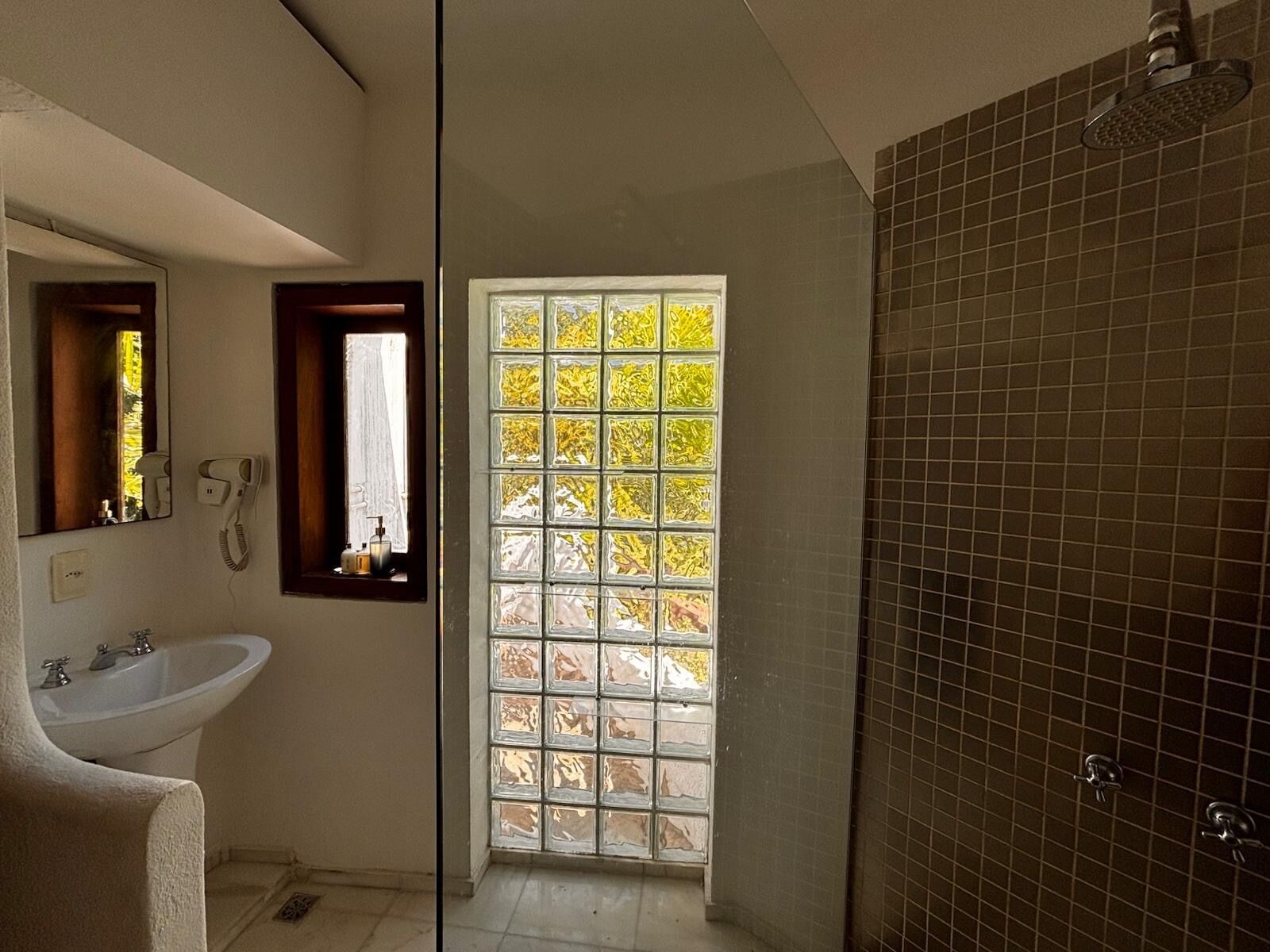 Un baño con un lavabo blanco, un espejo, un secador de pelo y una ducha con azulejos oscuros.
