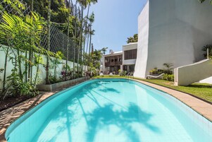 A swimming pool with a tiled edge, surrounded by greenery and a white building with a modern design.