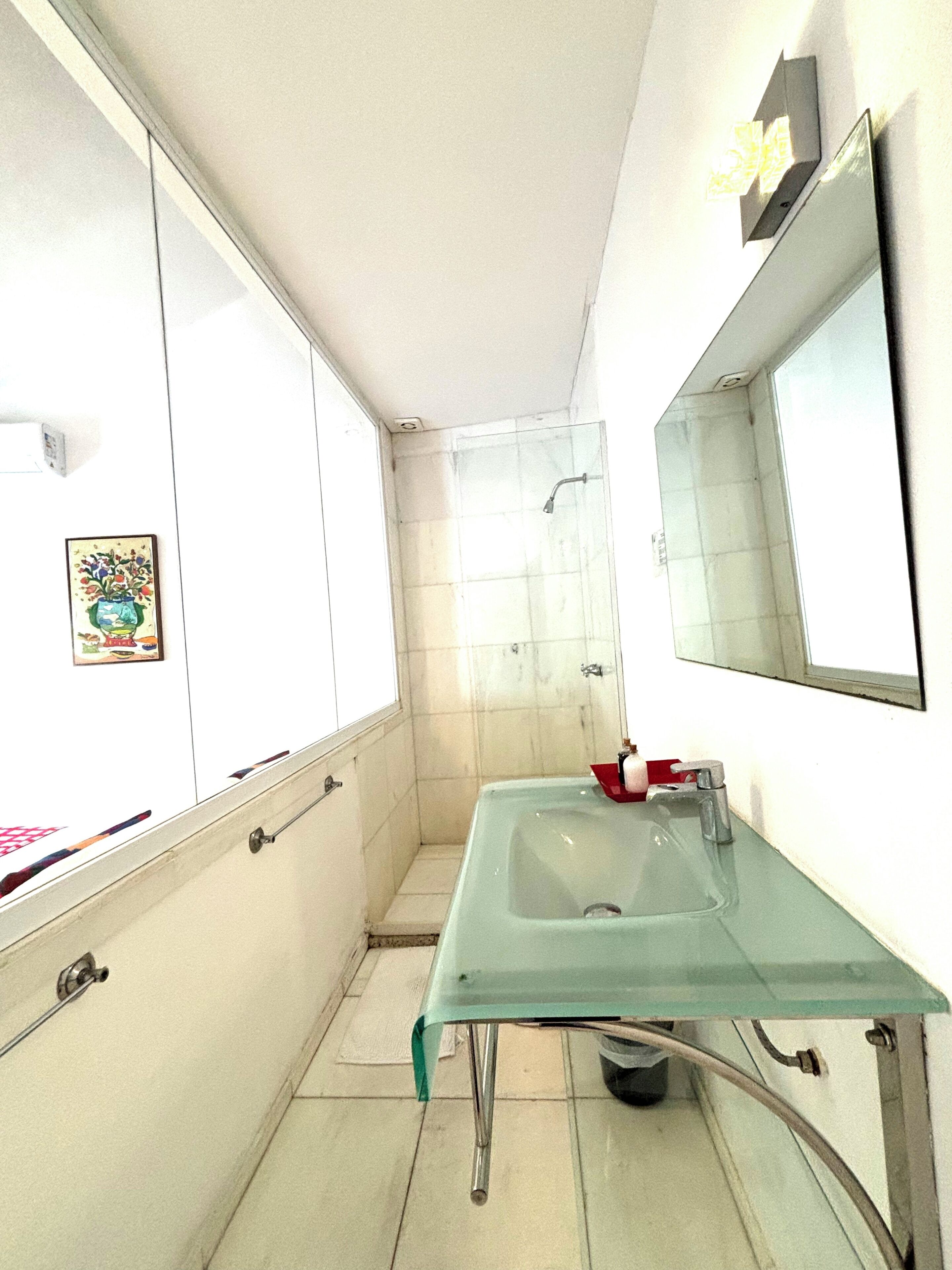 Un baño pequeño con un lavabo de vidrio, una ducha y un espejo en la pared.