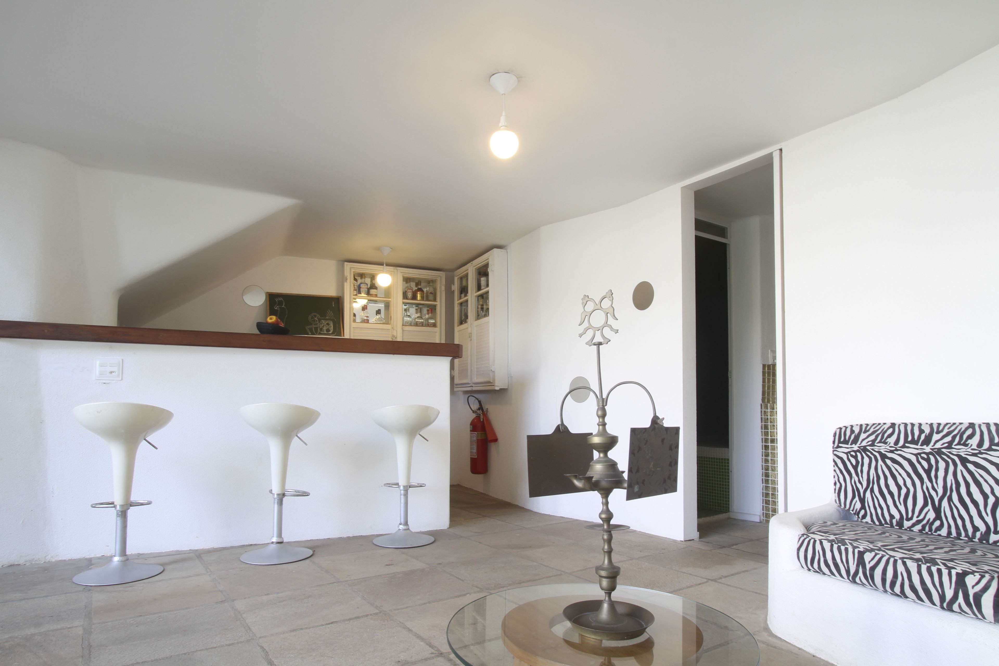 A modern living room with a glass coffee table, a zebra-patterned sofa, and three white bar stools.