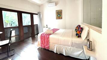 A bedroom with a bed, a desk, a chair, a window, and an air conditioning unit.