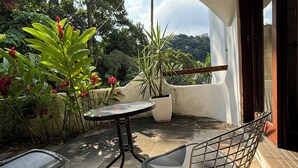 Eine Terrasse im Freien mit einem runden Tisch und zwei Stühlen, umgeben von Blumentöpfen und Grünpflanzen.