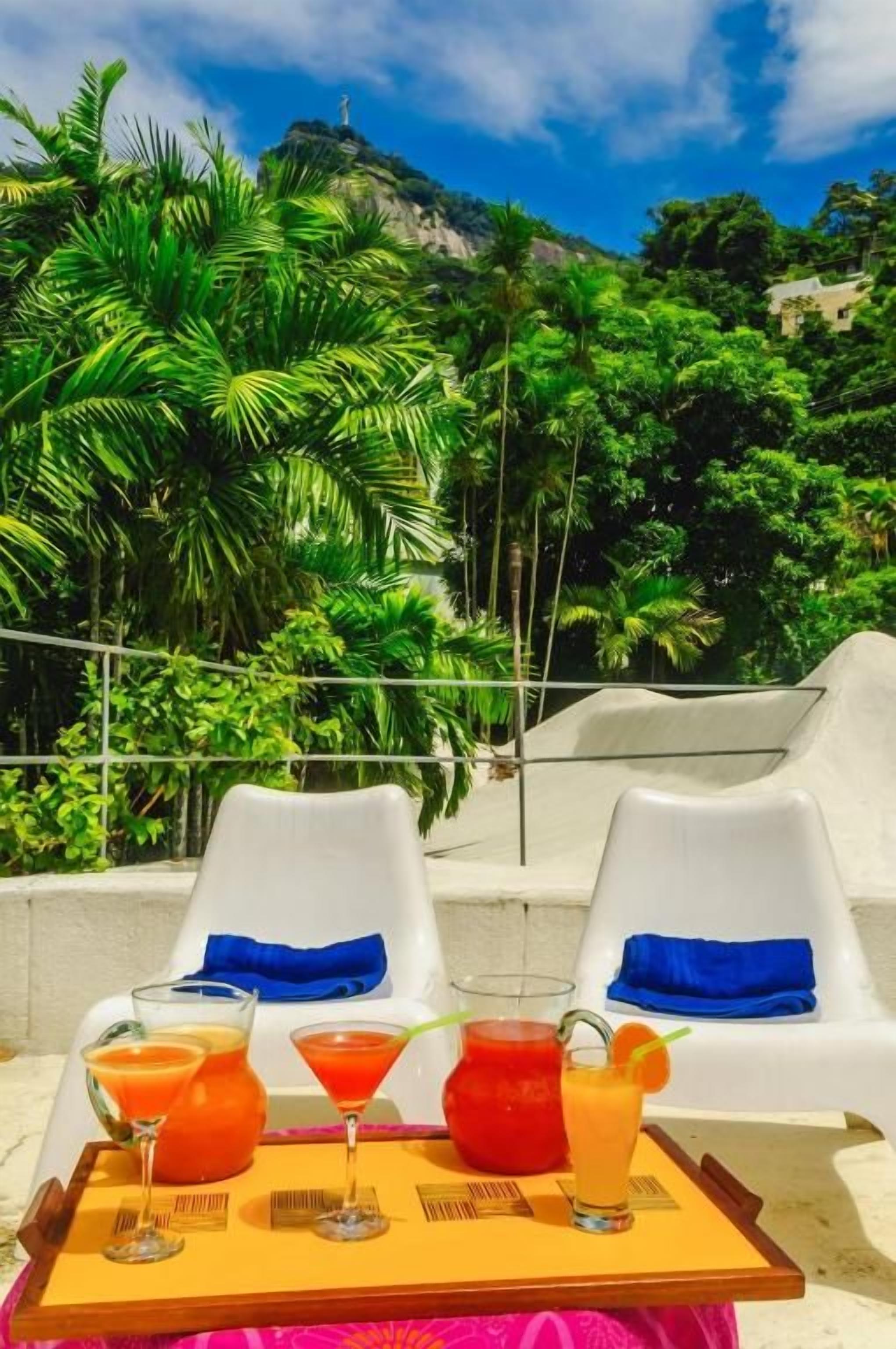 Une terrasse avec deux chaises blanches, un plateau avec des boissons et un décor luxuriant et verdoyant.