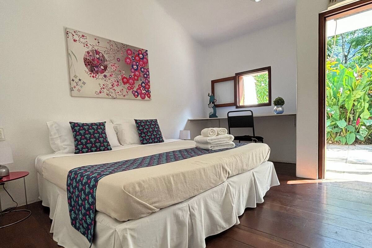 Un dormitorio con cama, mesita de noche y ventana con vista a follaje.