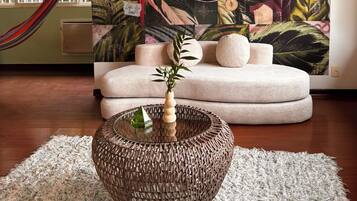 Una habitación con un cuadro grande de hojas tropicales, una mesa redonda tejida y una hamaca.