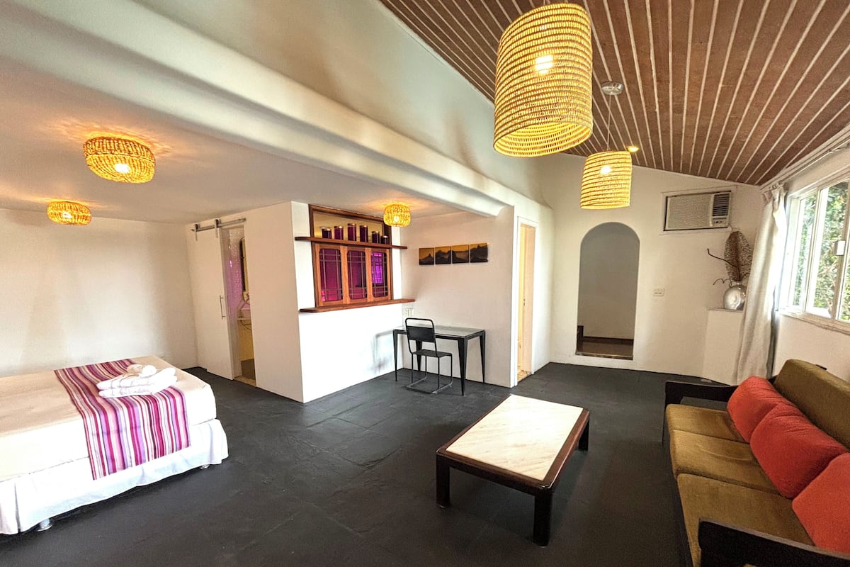 Una habitación con cama, sofá, una mesita y una pequeña cocina.