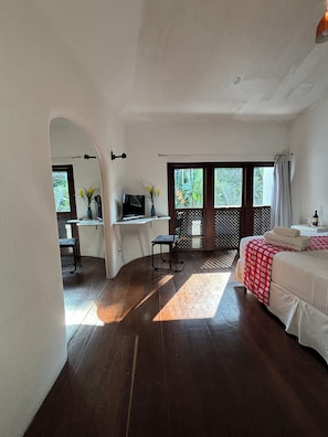 Quarto com cama, escrivaninha e televisão. Janela com vista para o verde.