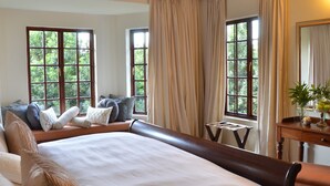 A hotel room with a large bed, two windows with curtains, a small table with a vase, and a mirror on the wall. - Highgrove House (Mbombela)
