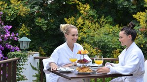 Two individuals seated at an outdoor table with breakfast items, surrounded by lush greenery. - Highgrove House (Mbombela)