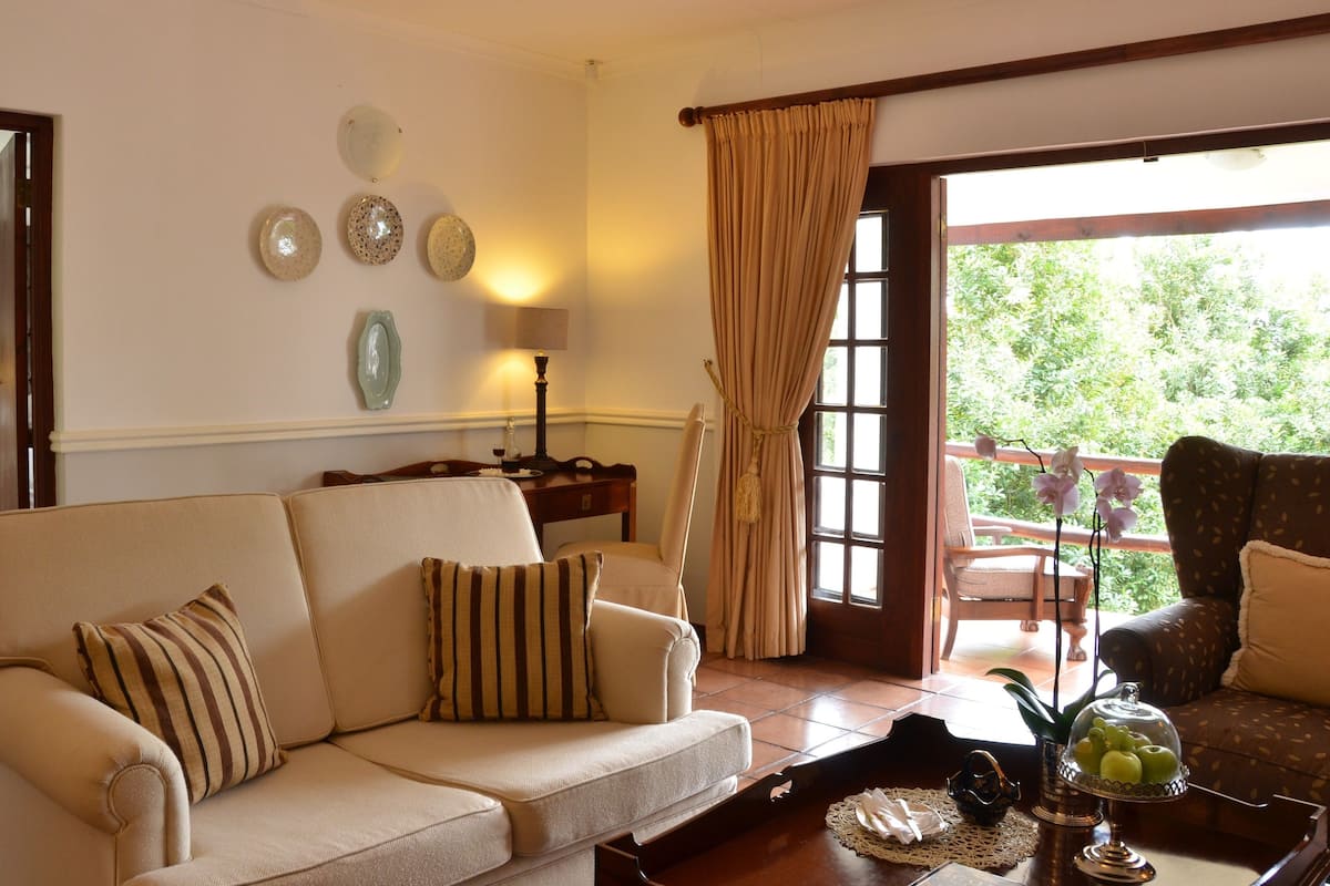 A living room with a sofa, a table with a fruit bowl, a lamp, and a view of a balcony with chairs.