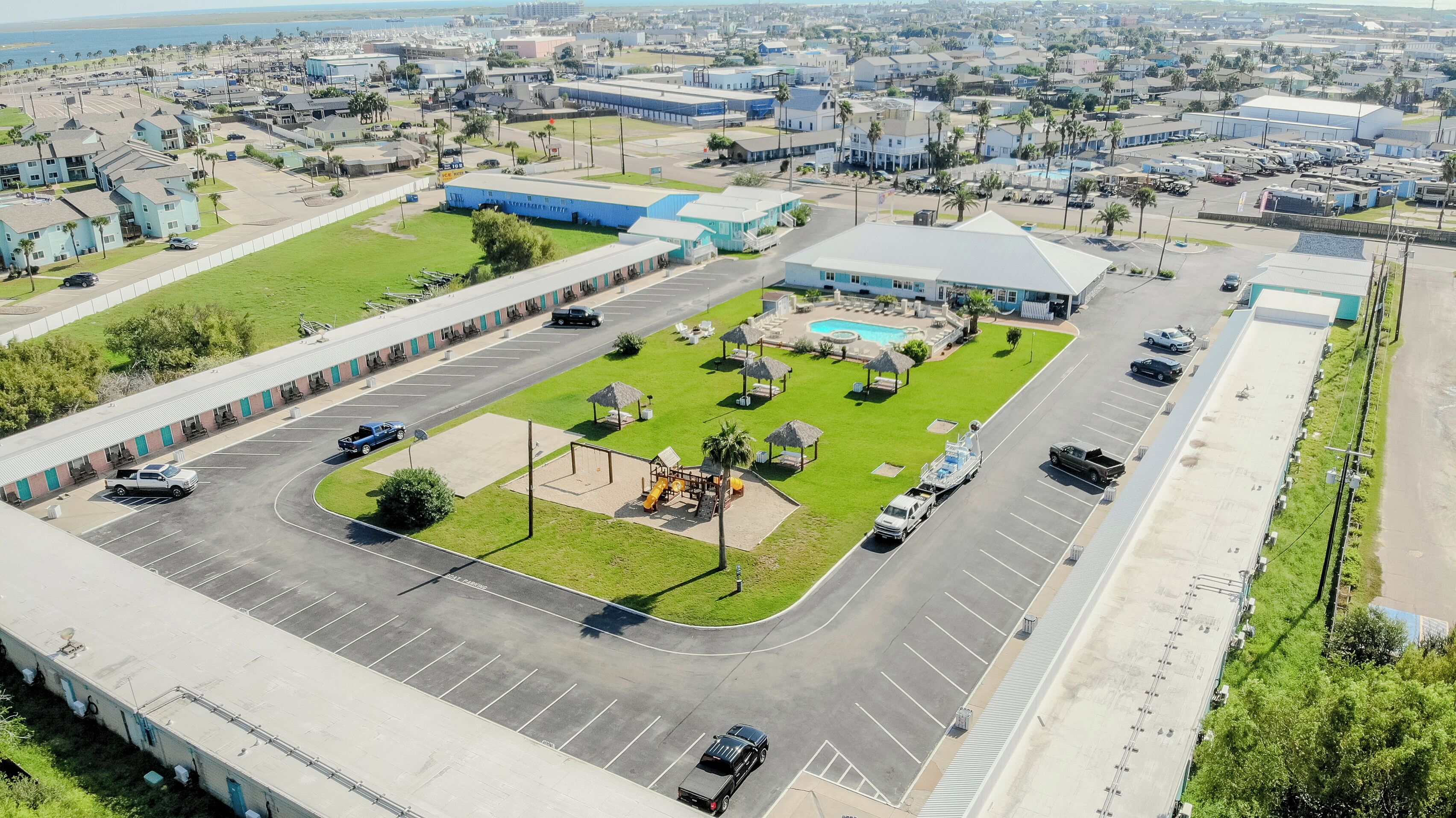 An aerial view of a parking lot with a swimming pool, a playground, and a large building with a flat roof.