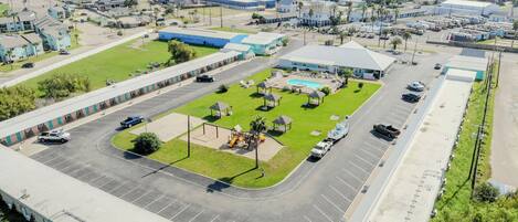 An aerial view of a parking lot with a swimming pool, a playground, and a large building with a flat roof.