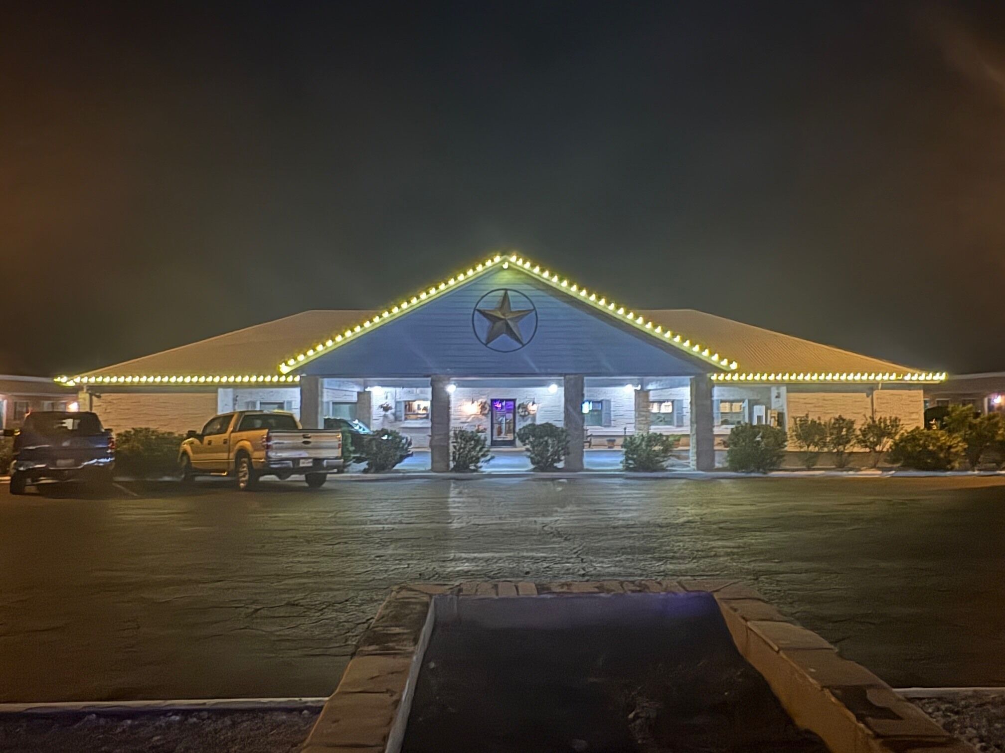 A building with a star emblem on the roof, a parking lot with a few vehicles, and a well-lit entrance.