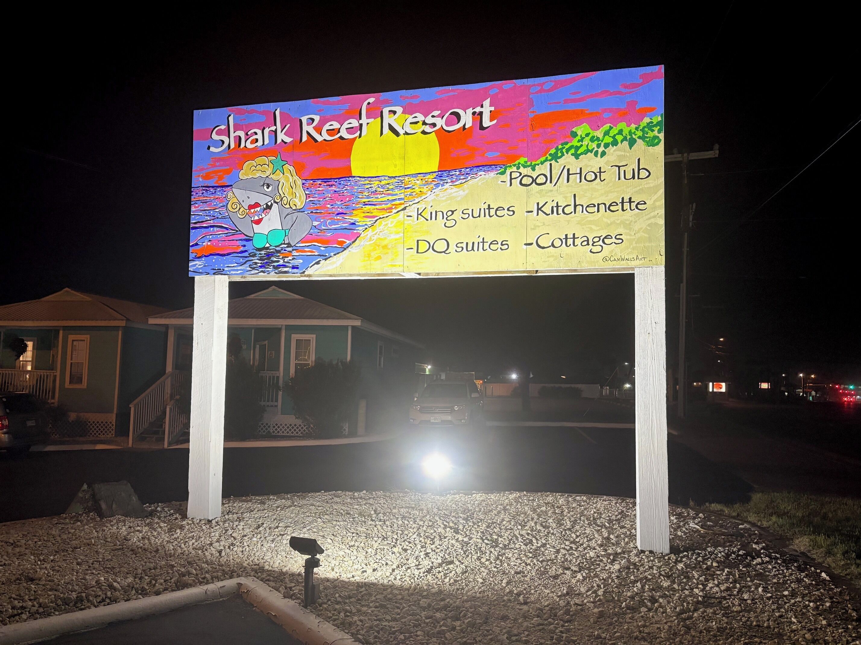 A nighttime signboard for Shark Reef Resort listing amenities like pool, hot tub, and various types of accommodations.