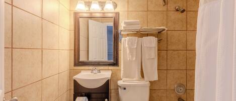 A bathroom with a sink, toilet, and bathtub. There are three lights above the mirror, and towels are stacked on a rack.