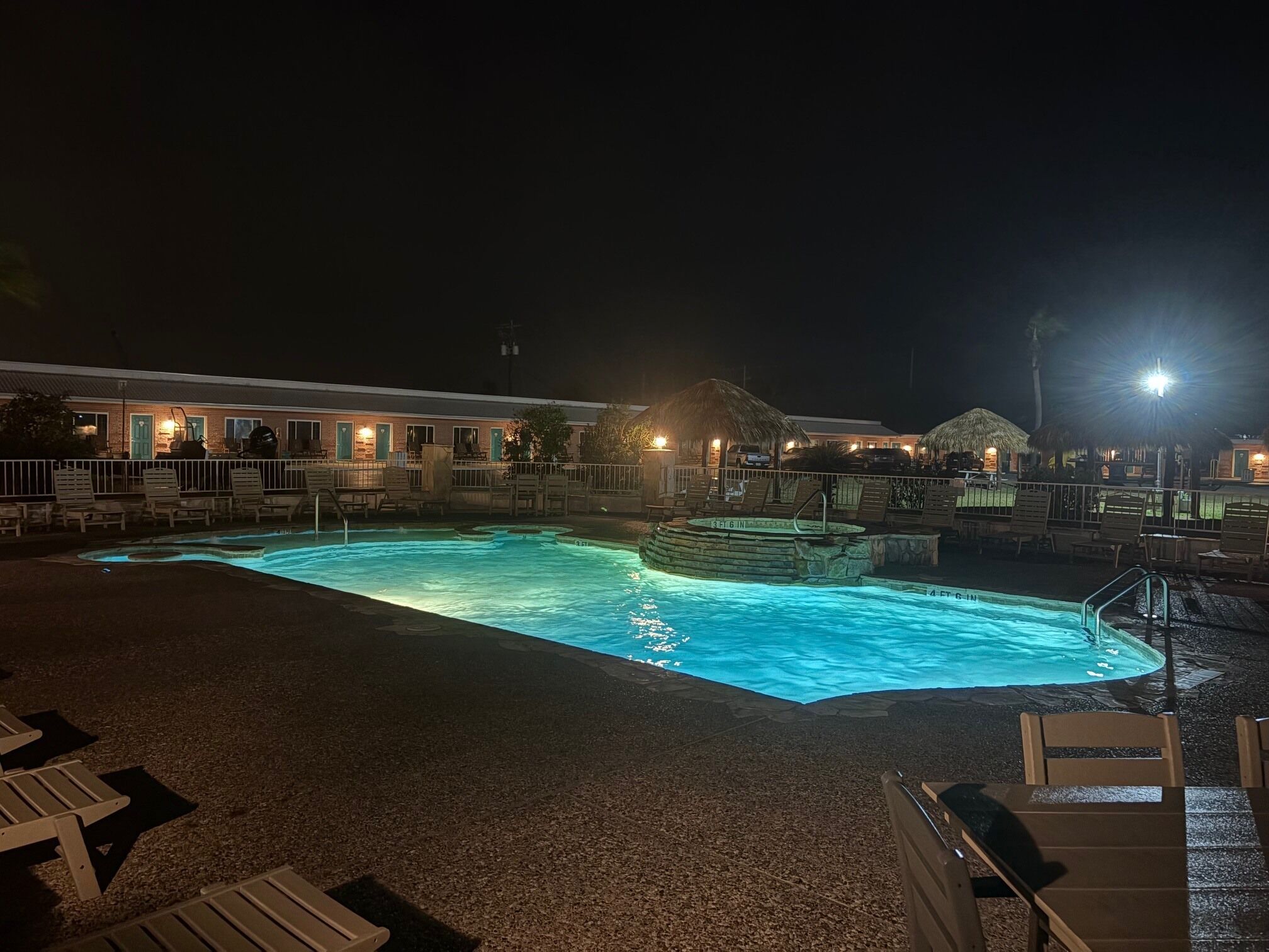 A nighttime pool area with lounge chairs and a hot tub.