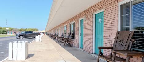 A row of wooden benches outside a building with teal doors and windows, a clear sky, and a parked SUV.