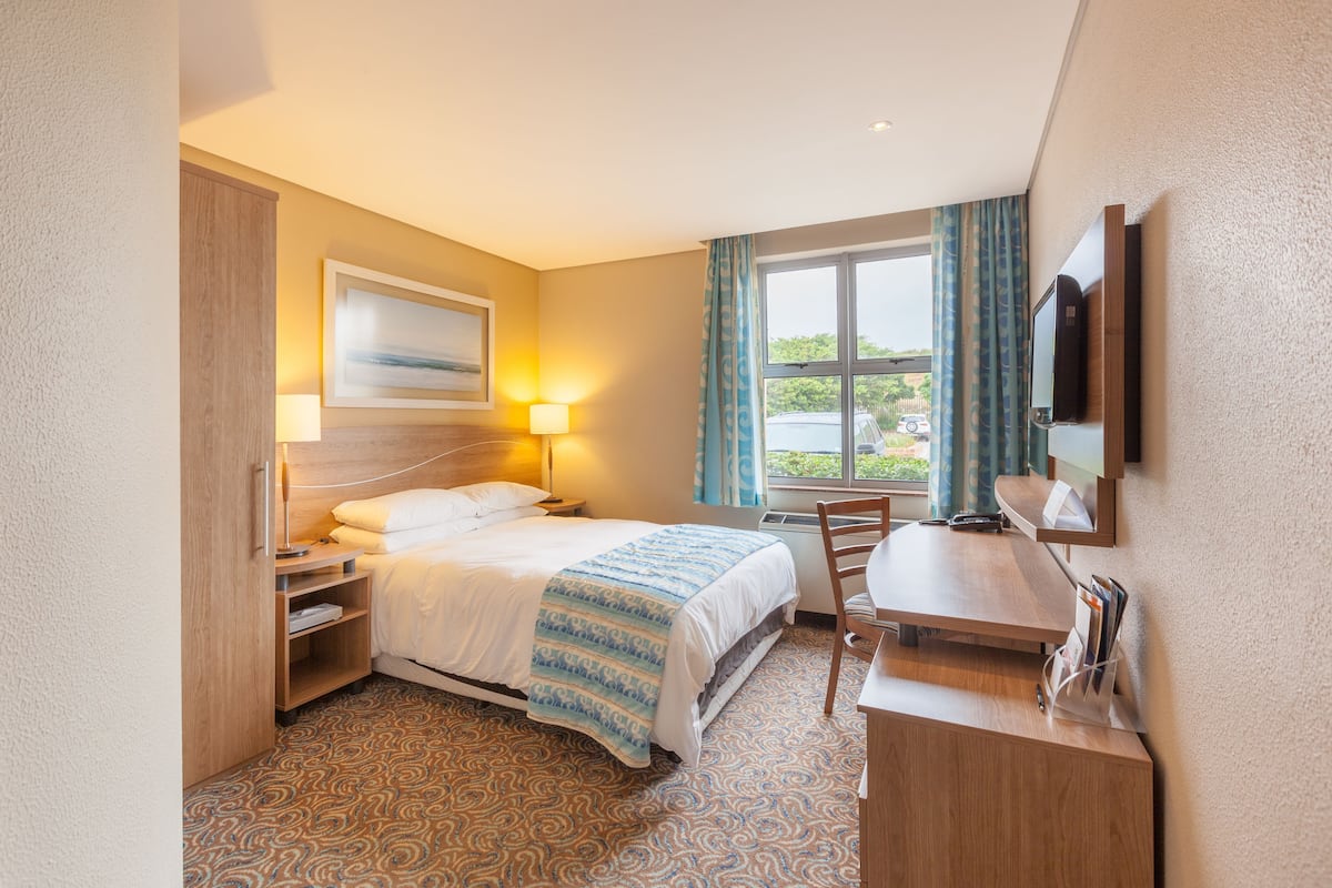 Habitación de hotel con cama, mesitas de noche, escritorio, silla, televisor y ventana con cortinas.