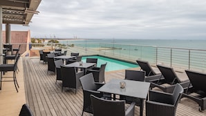 A deck with outdoor seating and a pool overlooking a beach.