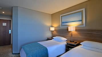 A hotel room with two beds, a painting of a beach, a nightstand with a lamp, and a door with a keycard lock.