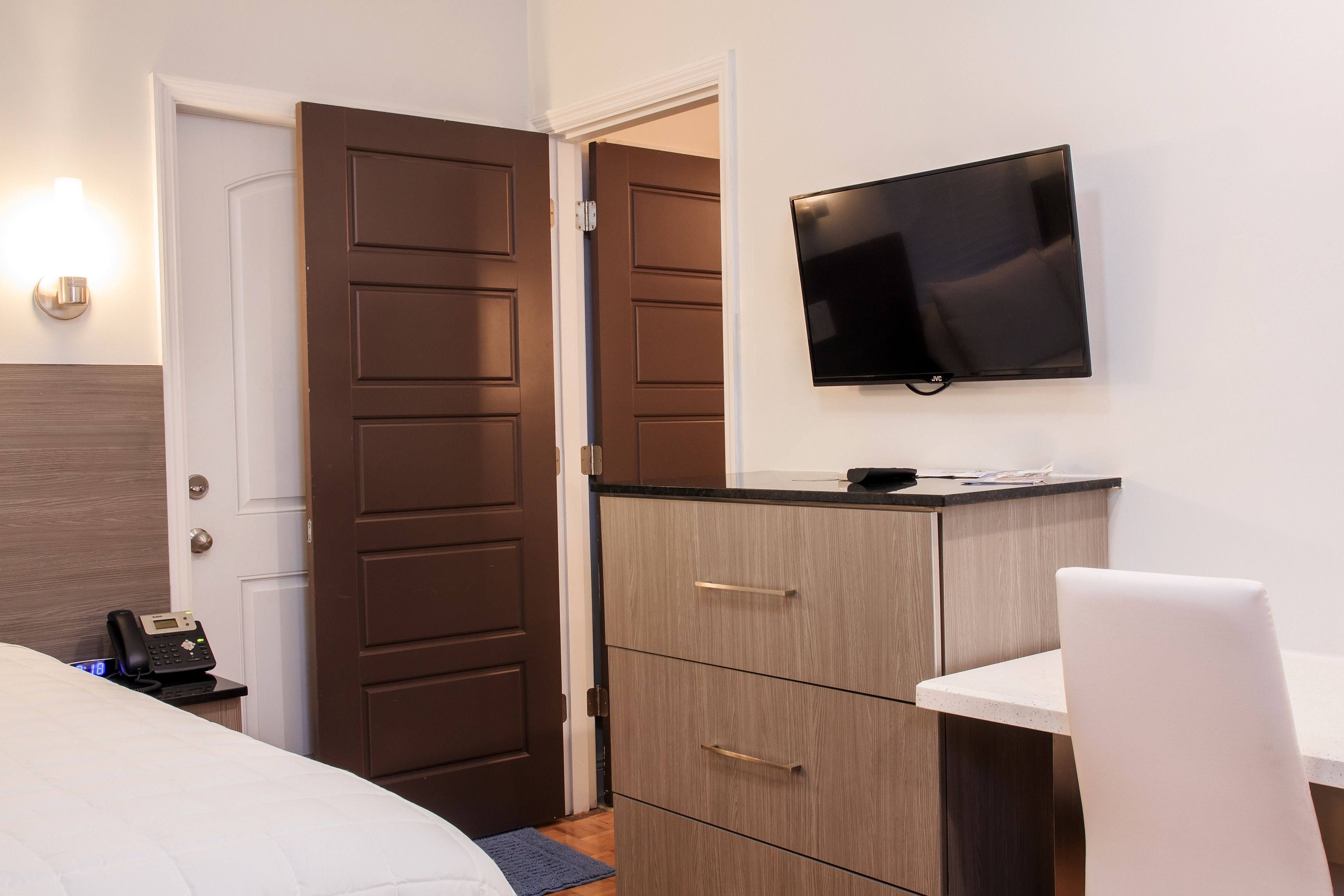 Une chambre d’hôtel comprenant un lit, un bureau avec une chaise, un téléviseur fixé au mur et une armoire.