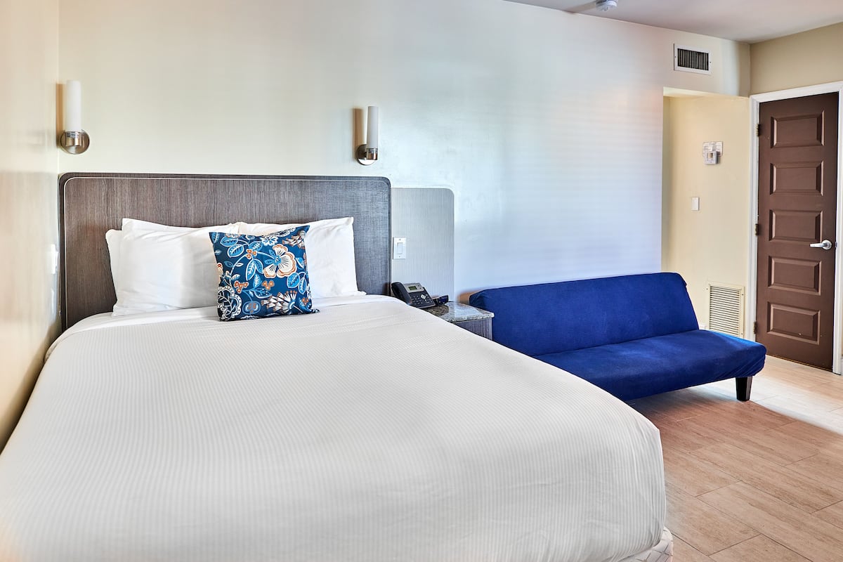 A hotel room with a large bed, a blue sofa, and a bedside table with a phone.